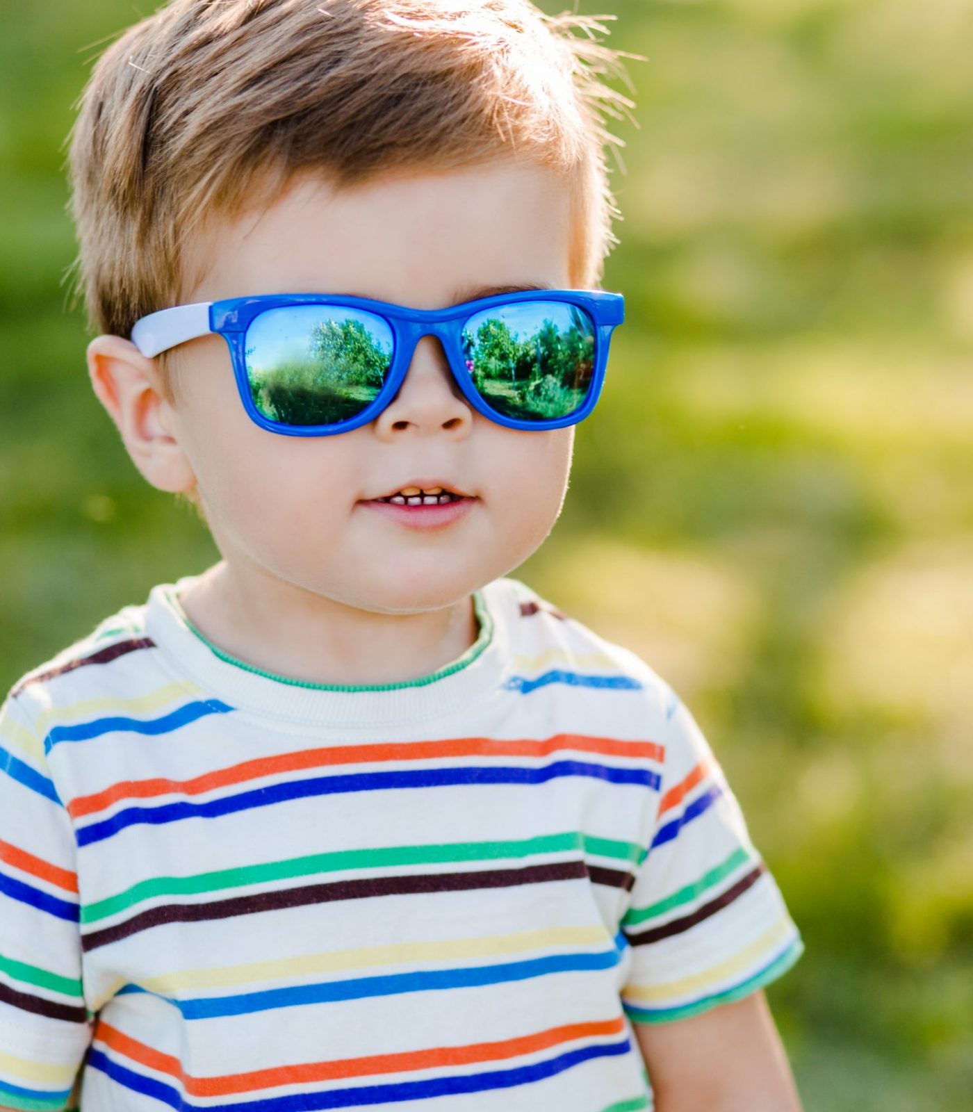 Litttle cute boy staying in the garden in bright sunglasses and smile